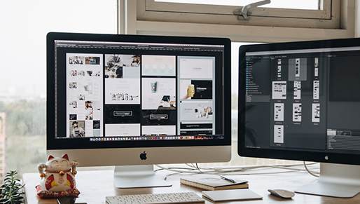 A desk setup with two monitors showing website design mockups.